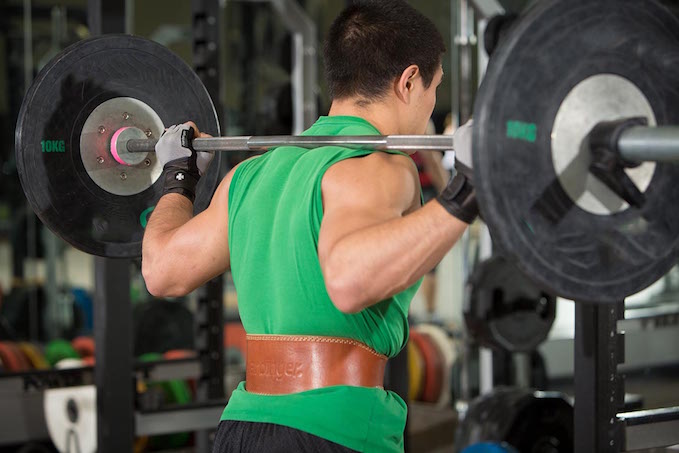 particante de musculação fazendo agachamento livre e usando um cinto como acessório de treino